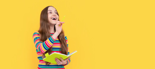 Happy kid genius got inspiration holding book and pointing pen up yellow background, idea. Banner of schoolgirl student. School child pupil portrait with copy space.