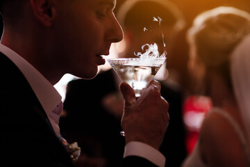On a festive wedding evening, young man drinks a martini poured into a triangular glass, a guy...