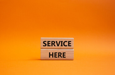 Service here symbol. Concept words Service here on wooden blocks. Beautiful orange background. Business and Service here concept. Copy space.