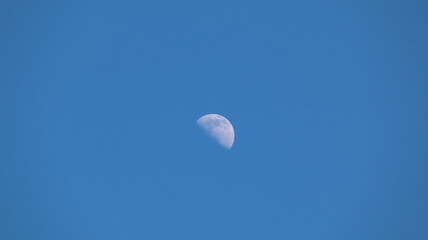 The moon shining in the daytime against the blue sky