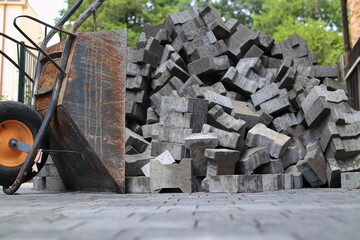Paving stones stacked on top of each other. There is a wheelbarrow next to it. - obrazy, fototapety, plakaty