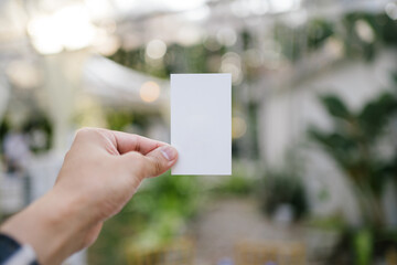 Hand holding a white card with the garden dinner blurry background