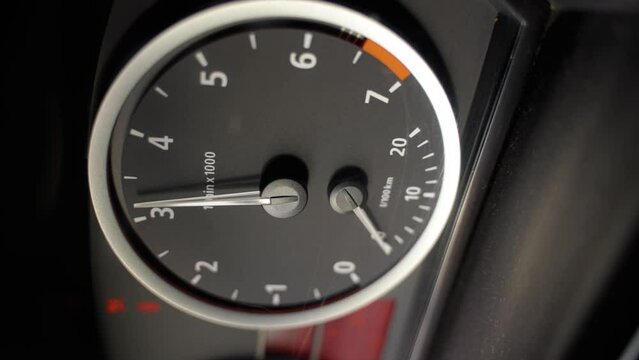 Black dashboard in a car. Tachometer circle. The tachometer needle moves and shows the engine speed. The red mark shows over-revving. Vertical video. Close-up