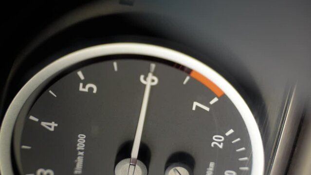 Dashboard in a car. The tachometer needle moves and shows the engine speed. The red mark shows over-revving. Vertical video. Close-up. Soft focus