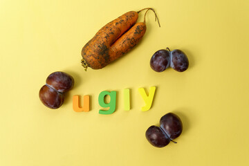 Ugly plums and carrot. Ugly fruit. Funny food. Trendy ugly food concept. Yellow bacground. Copy...