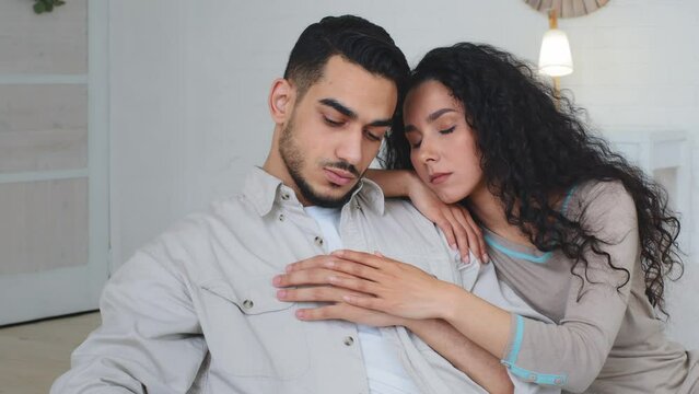 Sad couple upset offended Hispanic Indian bearded ill man stressful guy feeling resentment disappointed anxiety worried about mental disease Caucasian wife woman apologizing consoles supports husband
