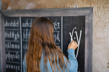 dziewczynka w niebieskiej bluzie pisze kreda po tablicy, stara szkoła retro klimat   - obrazy, fototapety, plakaty