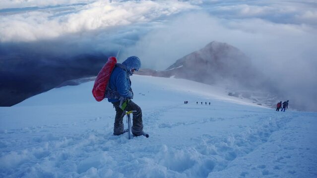 Hiker with backpacks reaches the summit of mountain peak.