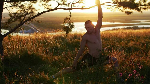 A muscular handsome shirtless man training on the field at sunset