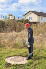 A man in overalls and a hard hat near a water well in the countryside. Inspection of water wells...