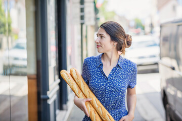 Young pretty woman buying a french baguette and standing on the street in city