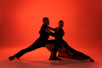 Silhouette of elegant couple dancing tango on red background
