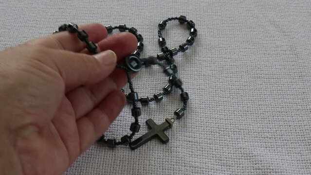 Female hands of an adult woman taking a rosary of hematite stone beads, praying the rosary to ask for the health of the sick and for peace in the world, shiny gray color. Concept of faith and hope