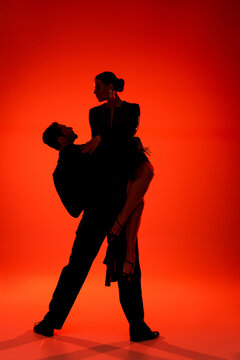 Silhouette of professional couple of dancers performing tango on red background