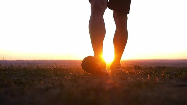 A muscular man holding jumping rope walks to a camera at sunset