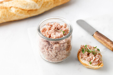 Toasts with tuna pate or rillettes on white board with baguette. Glass jar with fish rillettes....