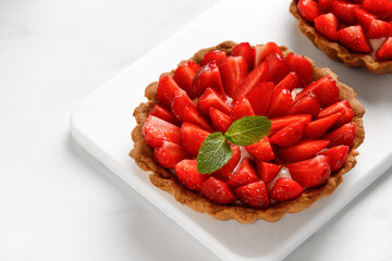 Tart with pieces of strawberry with vanilla cream on white board and white background, close up. Copy space