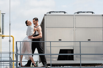 Stylish ballroom dancers performing choreography near railing on roof of building outdoors