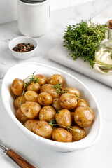 Roasted baby potatoes in white baked dish with thyme, close up.