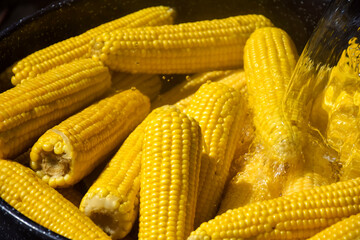 Process of cooking fresh mature corn. Sale of freshly boiled hot corn at fair. Natural yellow background. Close-up. Selective focus.