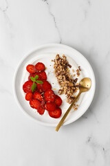 Delicious Breakfast with Yogurt,  strawberry and granola in white plate.  Creamy dairy product. Top view, marble background.