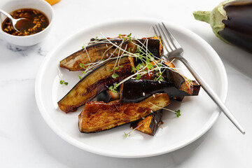 Fried eggplant sticks in the glaze with soy sauce and honey, garnished with microgreens, on white plate and white background, delicious vegetarian dish