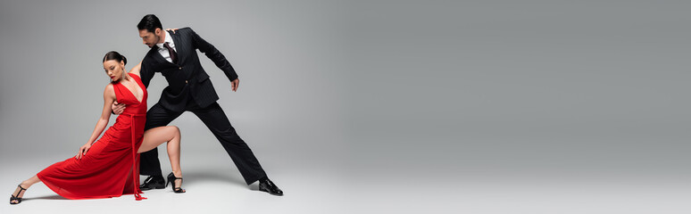 Stylish man in suit performing tango with woman on grey background, banner
