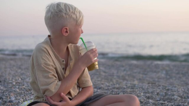 adorable teen boy with white hair drinks freshly squeezed juice on the background of the sea. Turkey, Alanya. High quality FullHD footage