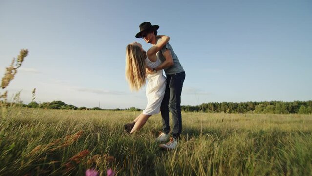Guy hugs blonde woman kissing on grass field under blue sky