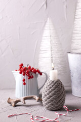 Winter decorations in grey, red and blue.. Burning  candle, jug with winter berries, horne, white holiday tree on grey textured background. Norven minimalistic style. Still life.
