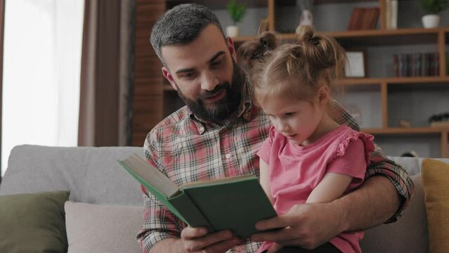 Young father and daughter read intersting book at home. Loving parent bearded man teaches his preschool child to read. Daddy reading fairy tale story. Parenthood, love and happy family concept.
