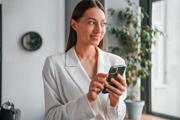 Using smartphone. Young beautiful woman in formal clothes is working at office