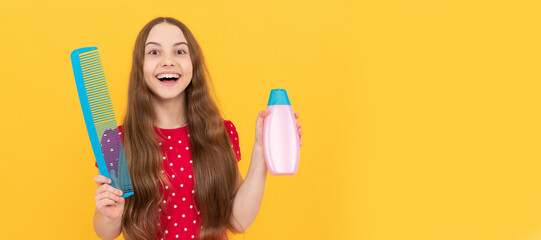 surprised child presenting shampoo and hairbrush for long hair on yellow background, beauty. Kid girl hair care, horizontal poster. Banner header with copy space.