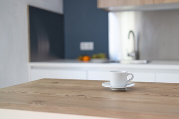 Cup of hot tea or coffee on a table in contemporary kitchen interior. Kitchen appliances and decor on background. Homemade bakery concept. Modern white furniture. 