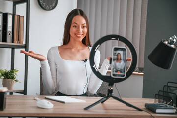 Talking, doing online master class. Young beautiful woman in white clothes is in the office