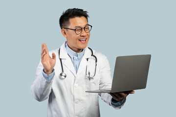 Happy middle aged chinese man therapist in white coat, glasses with laptop waving hand working remotely