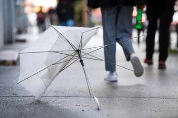 Abandoned white umbrella broken by the wind, left on the city street after a heavy storm. People...