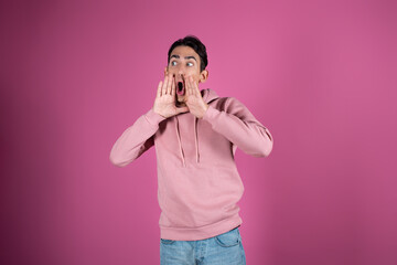 Emotional young man in a pink sweater on a pink background. Gestures by male hands.