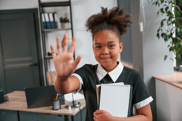 High five gesture. Cute little girl in school uniform is standing indoors in domestic room