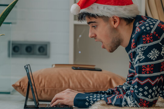 Young Man At Christmas At Home With Computer And Expression Of Surprise