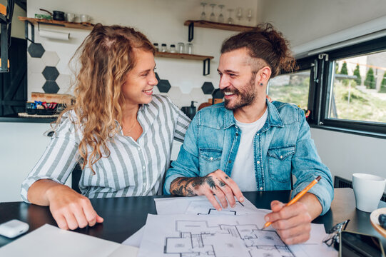Happy couple using laptop and looking into blueprints of their new home