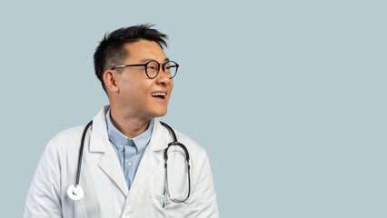 Fototapeta premium Smiling surprised middle aged chinese man doctor in white coat, glasses looks at empty space