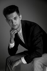 male portrait in black and white with a hand at the cheek sitting on chair man. isolated studio low-key lighting portrait. Classic male portrait in jacket and white shirt with a hand at the cheek