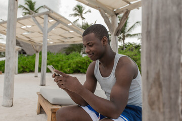 African american guy using mobile phone on bench in tropical terrace