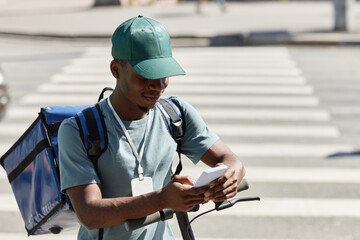 Portrait of young black man using smartphone while delivering food in city, copy space