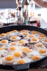 The company is having breakfast outside. Huge scrambled eggs with bacon in a frying pan close-up.