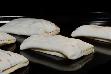 Fototapeta na wymiar Many uncooked puff pastry buns with red strawberry jam on tray in electric oven - close up view. Homemade bakery, food, cooking, pastry, semi-finished products and raw concept