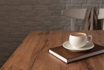 The concept of wishing a productive day. A cup of fragrant cappuccino on a wooden kitchen table. Still life in the style of minimalism. Horizontal photo. Selective focus. Place for text.