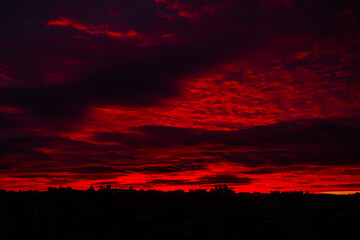 Obraz premium Colorful red sunrise over silhouette of city and dramatic sky with clouds - warm illumination, sun goes up. Nature, urban, morning, peaceful, atmospheric view concept