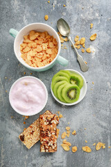 Tasty and healthy breakfast. Variety of food on kitchen table. Corn flakes, muesli bars and sliced kiwi fruits.